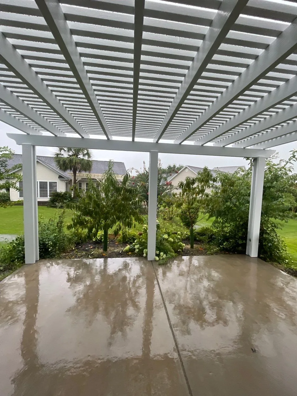 View from beneath a completed white pergola toward its posts and a Surfside Beach garden