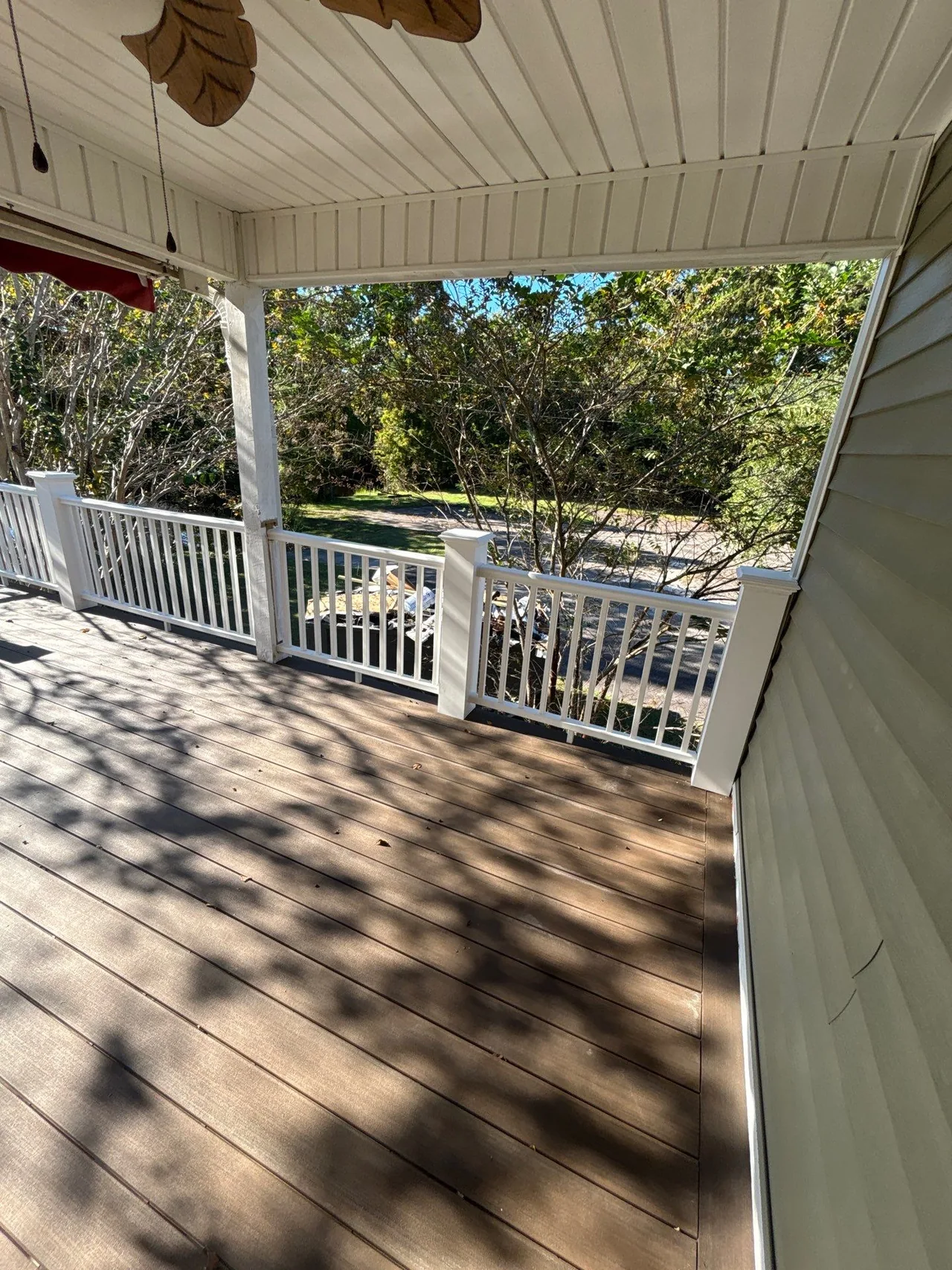 Brown-toned installed deck boards beneath a covered porch beside white rails and trees.