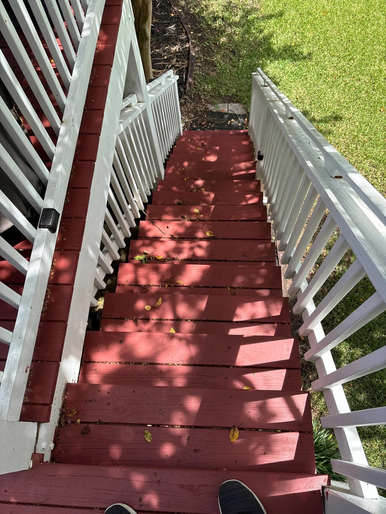 Leaves and small debris on the original red-painted porch steps beside white rails.