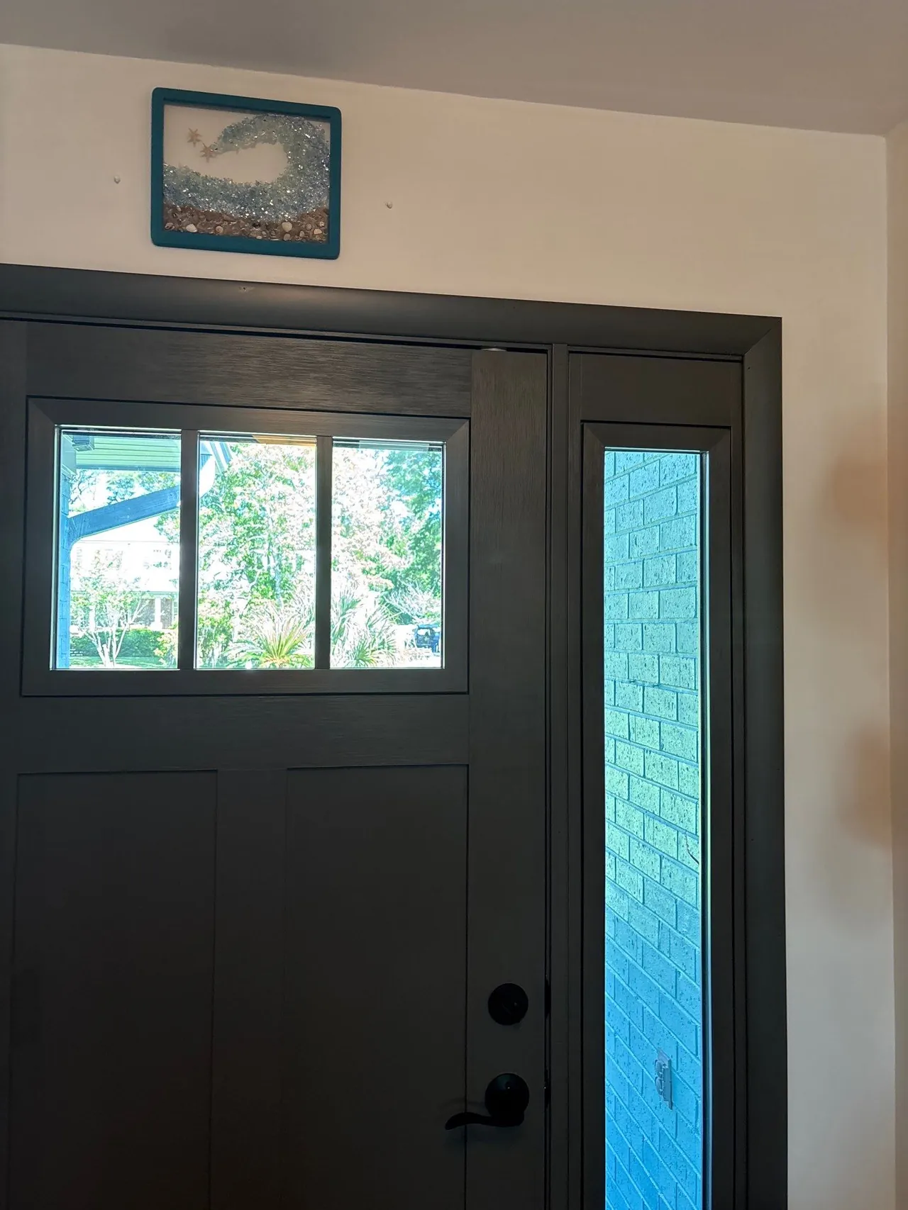 Interior view of the new dark entry door with upper glass panels and a narrow sidelight