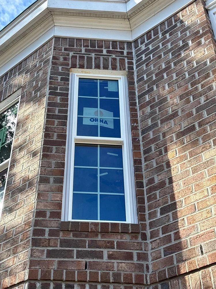 A white-framed replacement window with grid lines in a brick exterior during installation
