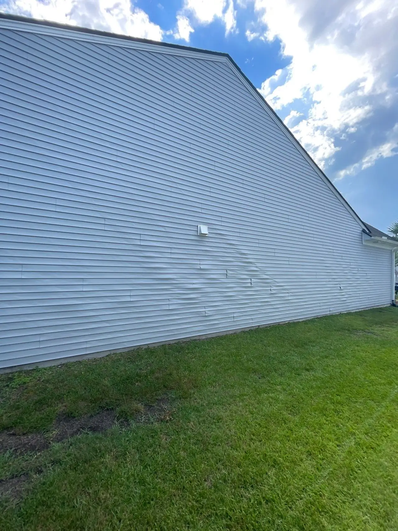 Original light-colored siding with visibly distorted lower courses on a Carolina Forest home.