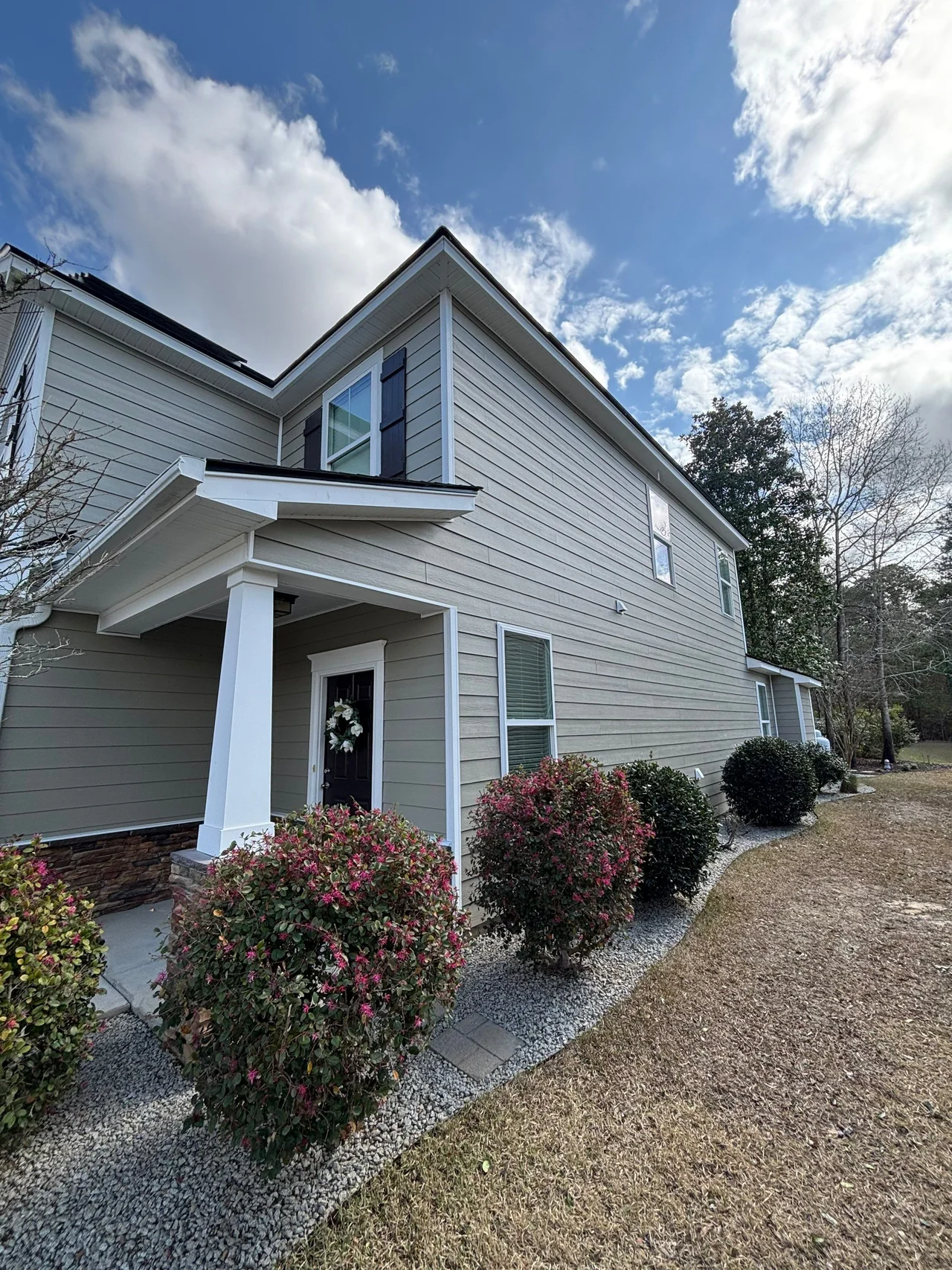 Taupe horizontal lap siding beside a white-trimmed entry porch and established shrubs