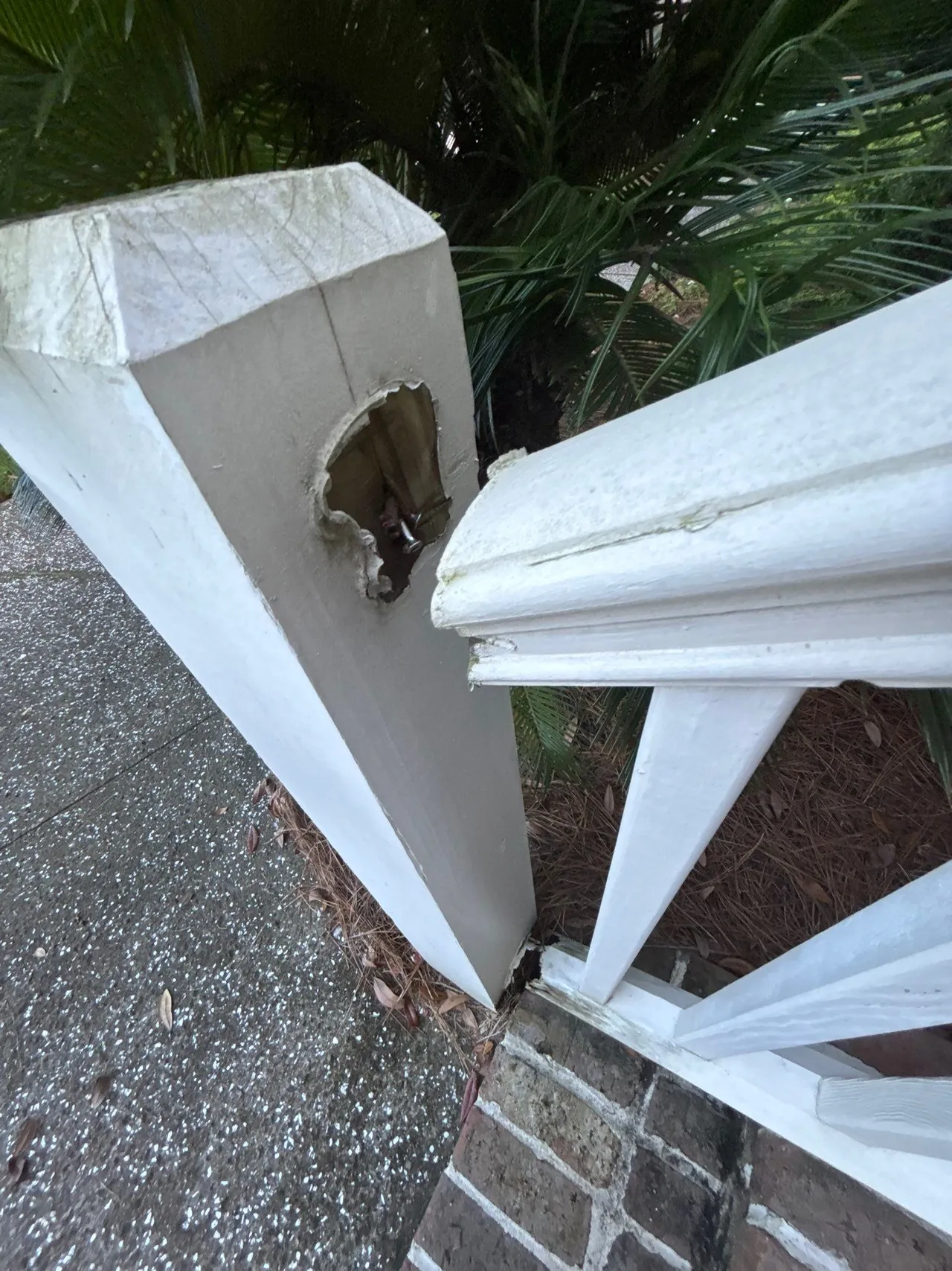 Opening in an existing painted wood railing post beside a brick step